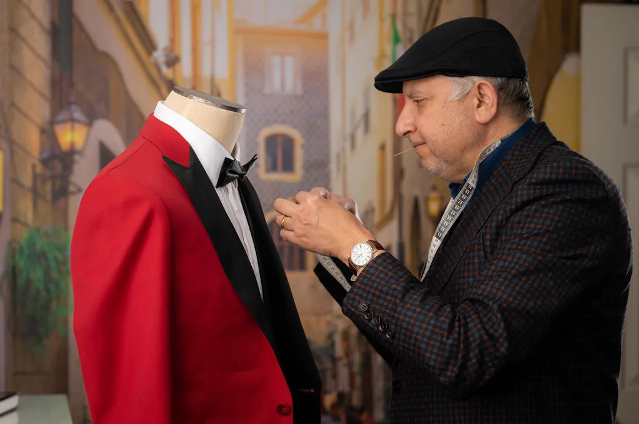 Sam pinning a red dinner jacket with a black shawl lapel on the dress form, tape measure round his neck